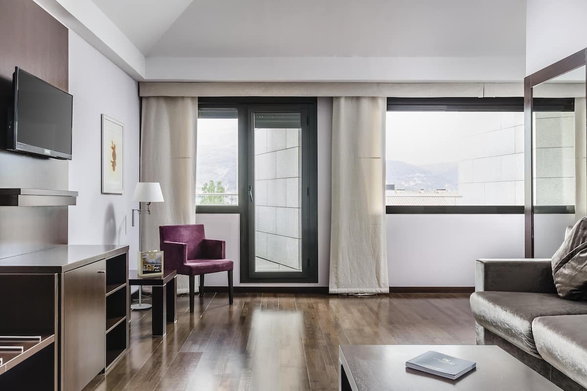 Een moderne hotelkamer met een groot raam, een flatscreen televisie, een bank, een stoel en een klein tafeltje.
