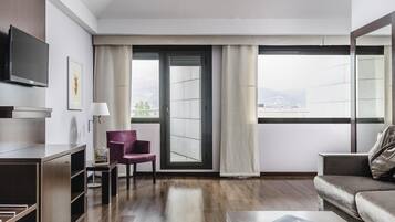 Una habitación de hotel moderna con un ventanal grande, un televisor de pantalla plana, un sofá, una silla y una mesita.