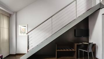 A modern room with a wooden floor, a staircase with metal railings, a desk with a chair, and a flat-screen TV mounted on the wall.