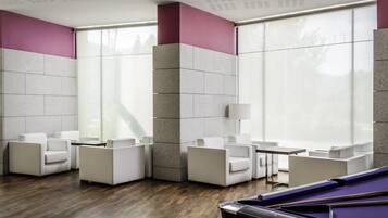 A modern lounge with white sofas, a pool table, and large windows.