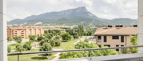 Un balcón con vistas a un paisaje montañoso, un estacionamiento y un edificio de fachada roja.