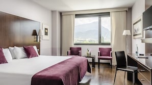 Une chambre d’hôtel avec un grand lit, deux fauteuils, un bureau et une télévision.