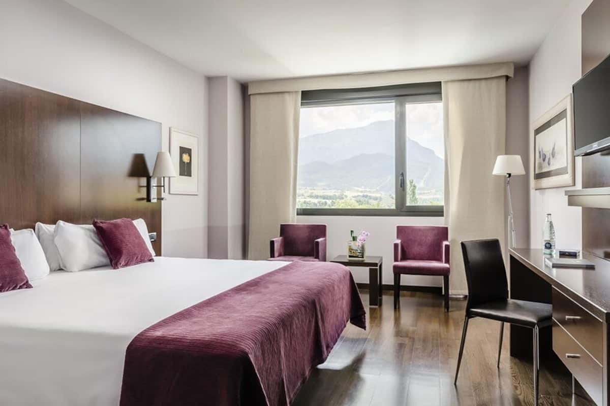 Een hotelkamer met een groot bed, twee stoelen, een bureau en een televisie.