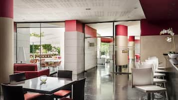 A modern hotel lobby with a glass partition, red and white decor, and a seating area with tables and chairs.