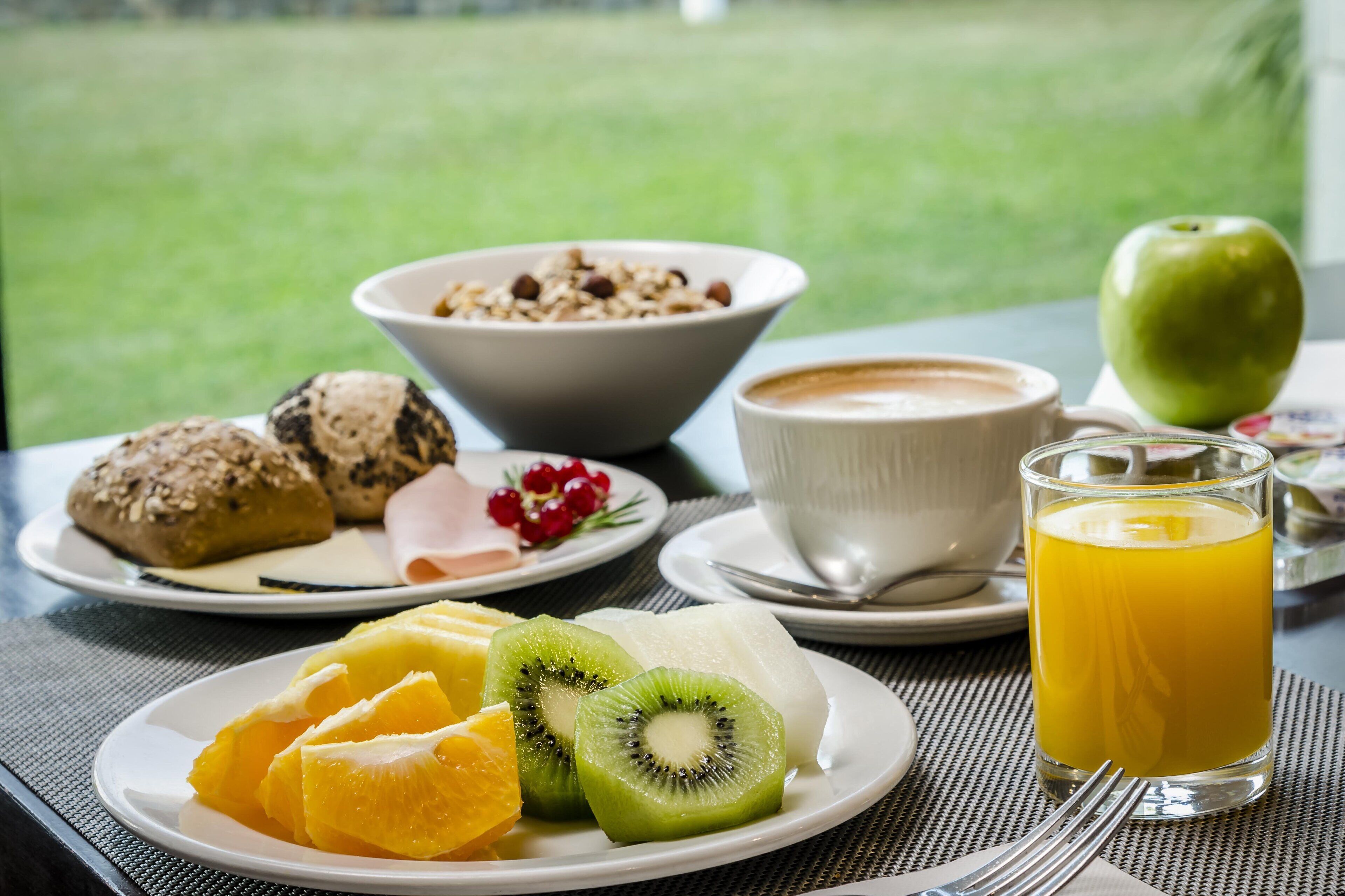 Un desayuno con platos de fruta, pasteles, una taza de café y un vaso de zumo de naranja.