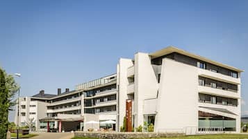 A modern multi-story hotel with a flat roof, large windows, and a covered outdoor seating area.
