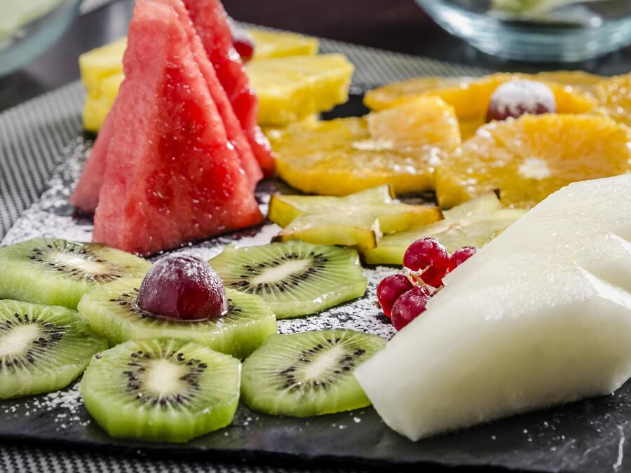 Una variedad de frutas frescas, como sandía, kiwi, uvas y trozos de piña, dispuestas sobre un plato de pizarra.