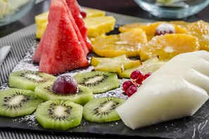 Eine Auswahl frischer Früchte, darunter Wassermelone, Kiwi, Trauben und Ananasstücke, drapiert auf einer Schieferplatte.