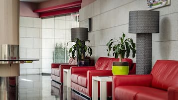 A modern lobby with red leather sofas, a glass coffee table, and potted plants.