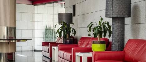 A modern lobby with red leather sofas, a glass coffee table, and potted plants.