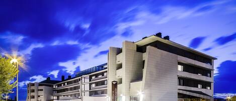 A modern hotel with a multi-story structure, outdoor seating area, and a well-lit entrance.
