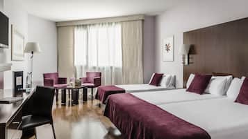 Habitación de hotel con dos camas, un escritorio, una silla, un televisor y una ventana con cortinas.