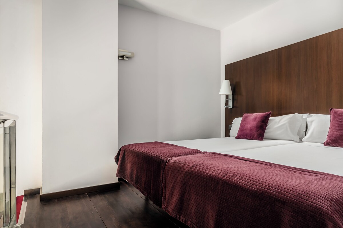 Ein Hotelzimmer mit einem großen Bett, einem Holzkopfteil, einem Nachttisch und einem Beistelltisch.