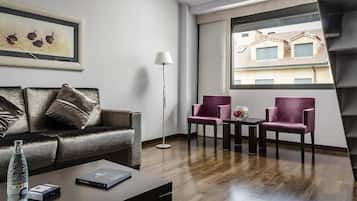 Una sala de estar moderna con un sofá de cuero oscuro, dos sillones morados, una mesa de centro y una lámpara de pie. Un cuadro enmarcado cuelga de la pared, y una ventana ofrece vistas a edificios.