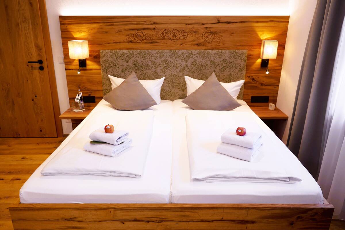 A double bed with two pillows, a wooden headboard, bedside lamps, and a small table with a glass and a bottle.