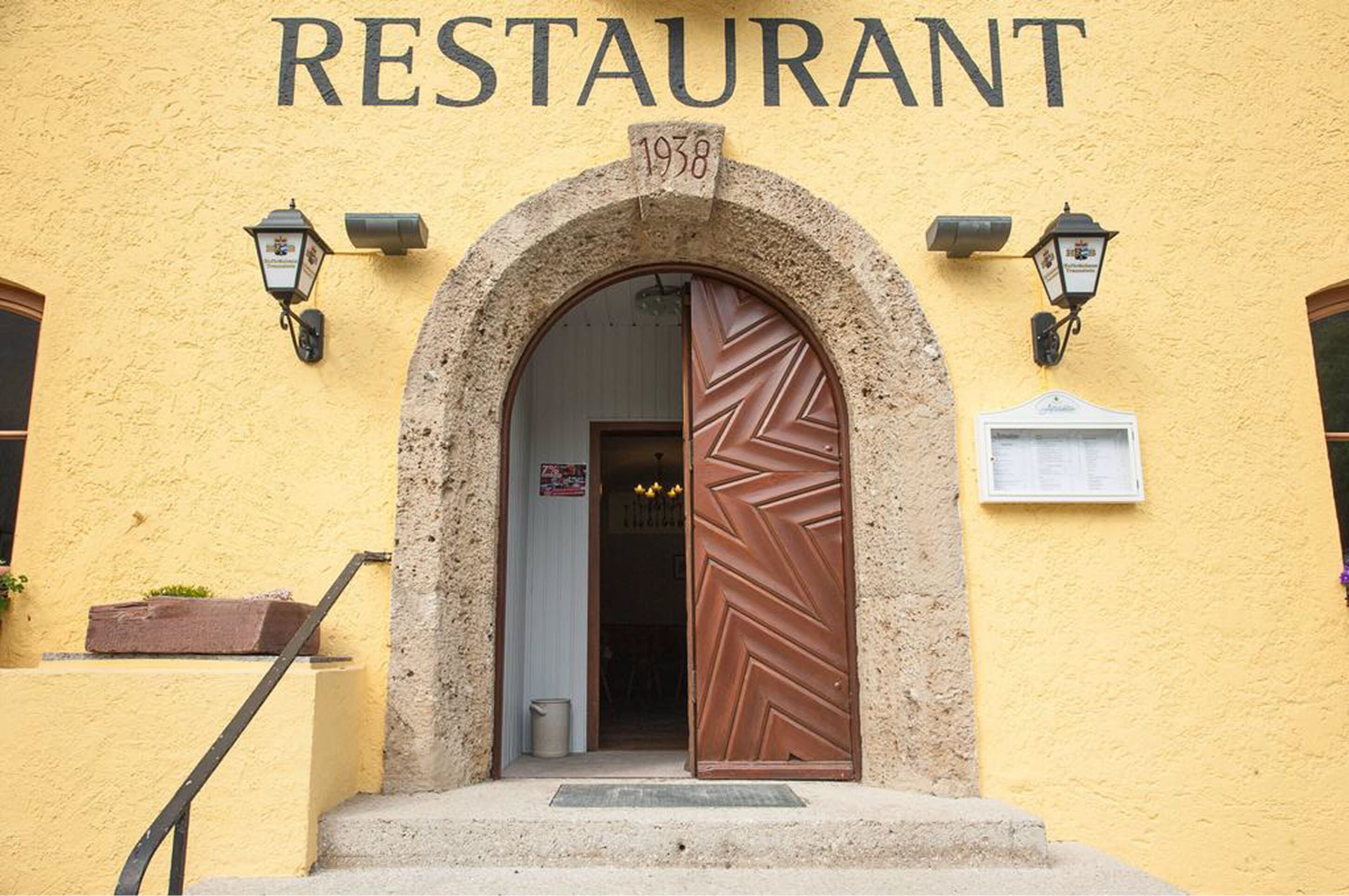 Een restaurant met een geel gevel, een boogvormige ingang en een grote houten deur.