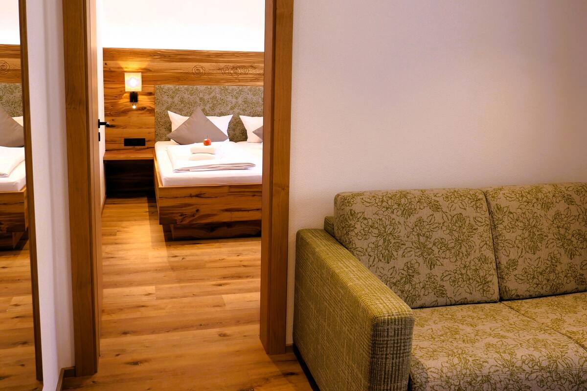A wooden-floored room with a bed, a sofa, and a nightstand.