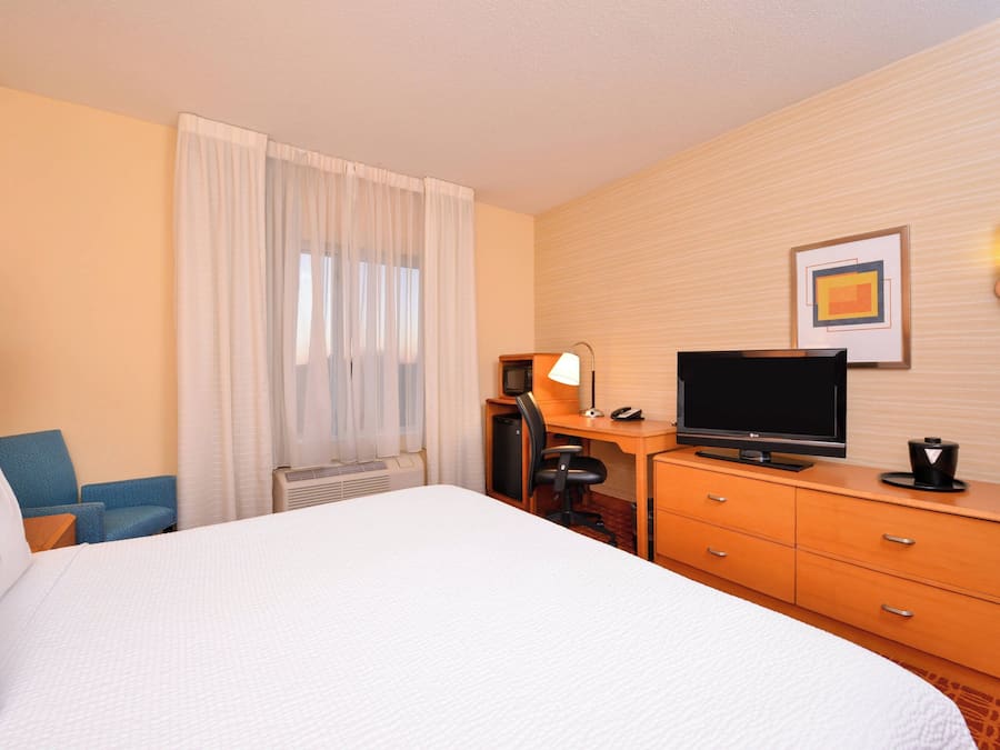 A hotel room with a large bed, a desk with a computer, a television, and a chair.
