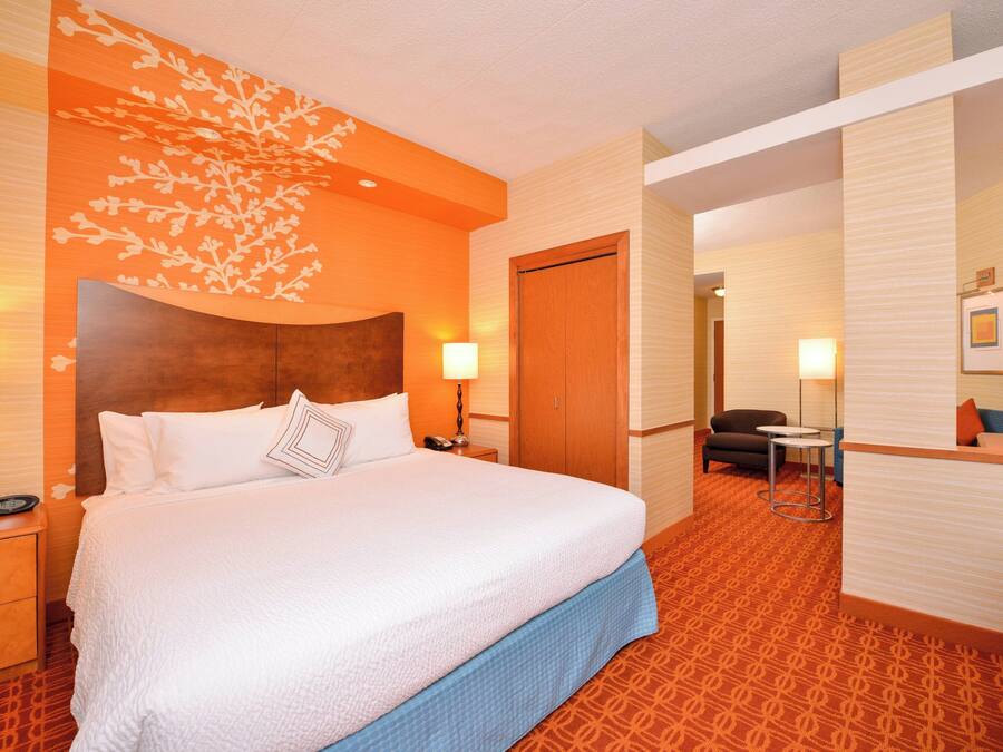 A hotel room with a large bed, a wooden headboard, a desk with a chair, and a patterned carpet.