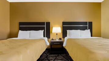 A hotel room with two beds, a nightstand with a lamp, and a patterned carpet.