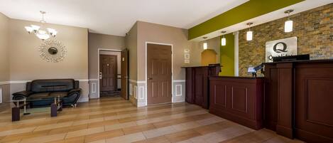 A spacious lobby with a wooden floor, a leather sofa, a chandelier, and a reception desk with a sign.