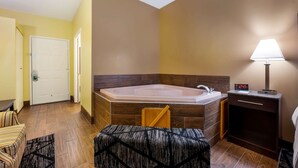 A bathroom with a large bathtub, a sink, a clock, and a small table with a chair. - Quality Inn Fort Payne (Fort Payne)