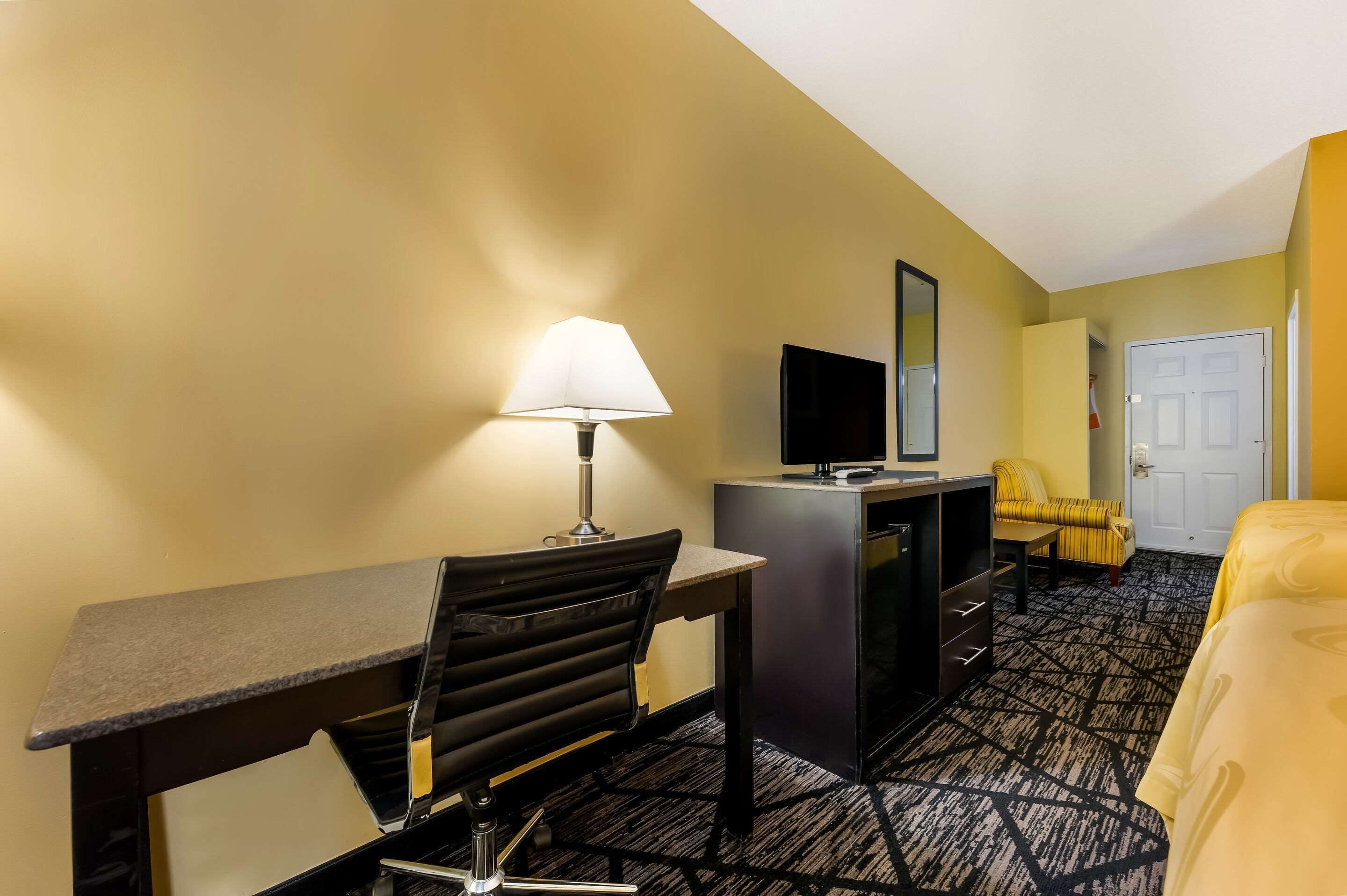 A hotel room with a desk, chair, bed, and a television.