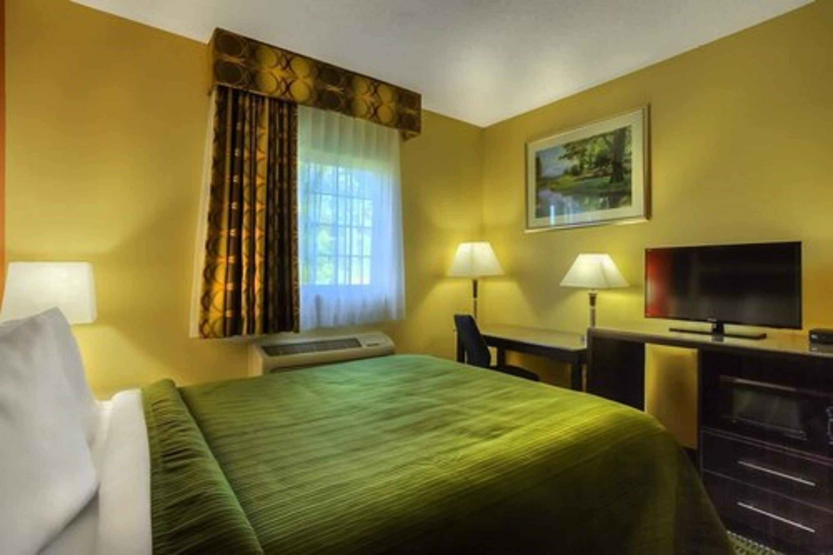 A hotel room with a bed, a desk, a television, and a painting on the wall.