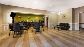 A spacious room with a dining area featuring a long table and chairs, a sofa, and a television mounted on the wall. - Quality Inn Fort Payne (Fort Payne)
