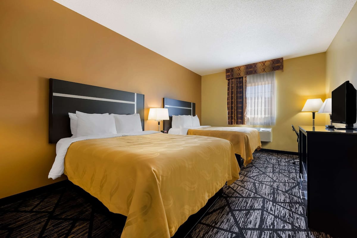 A hotel room with two beds, a desk, a TV, and a window with curtains.