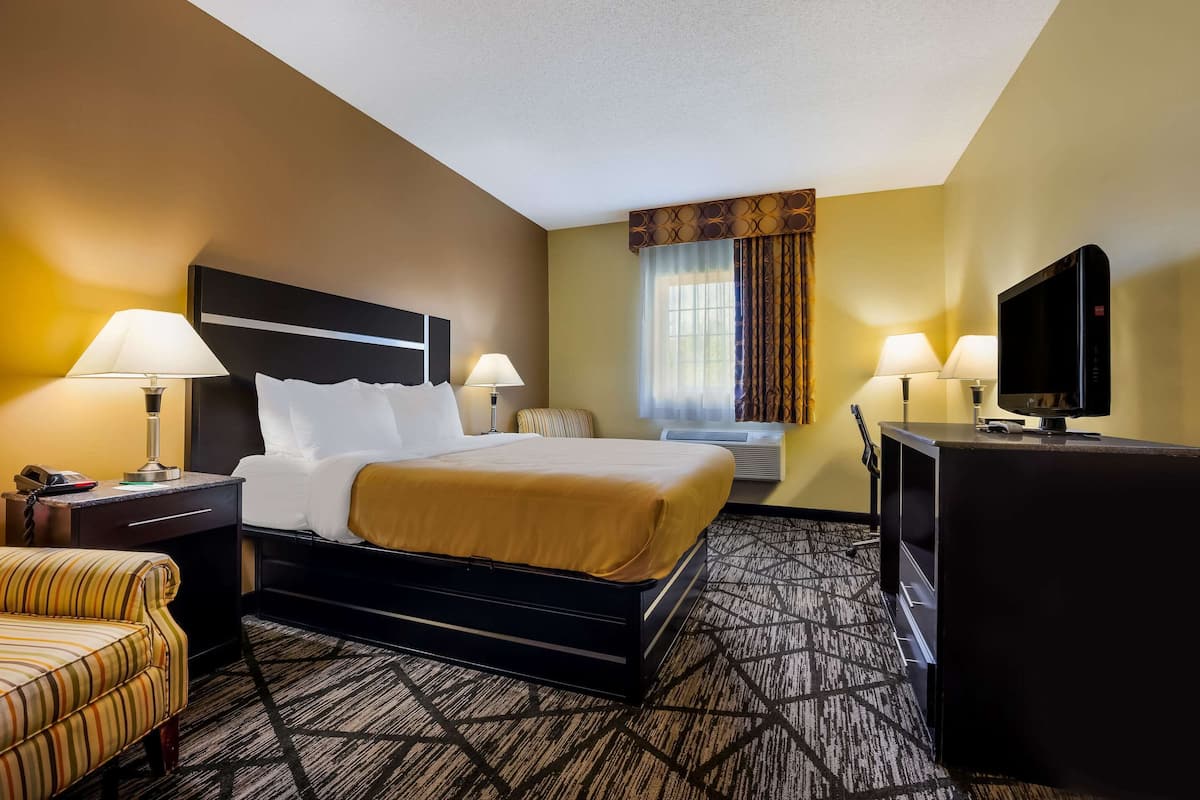 A hotel room with a bed, two bedside lamps, a television, a desk with a lamp, a chair, and a window with curtains.