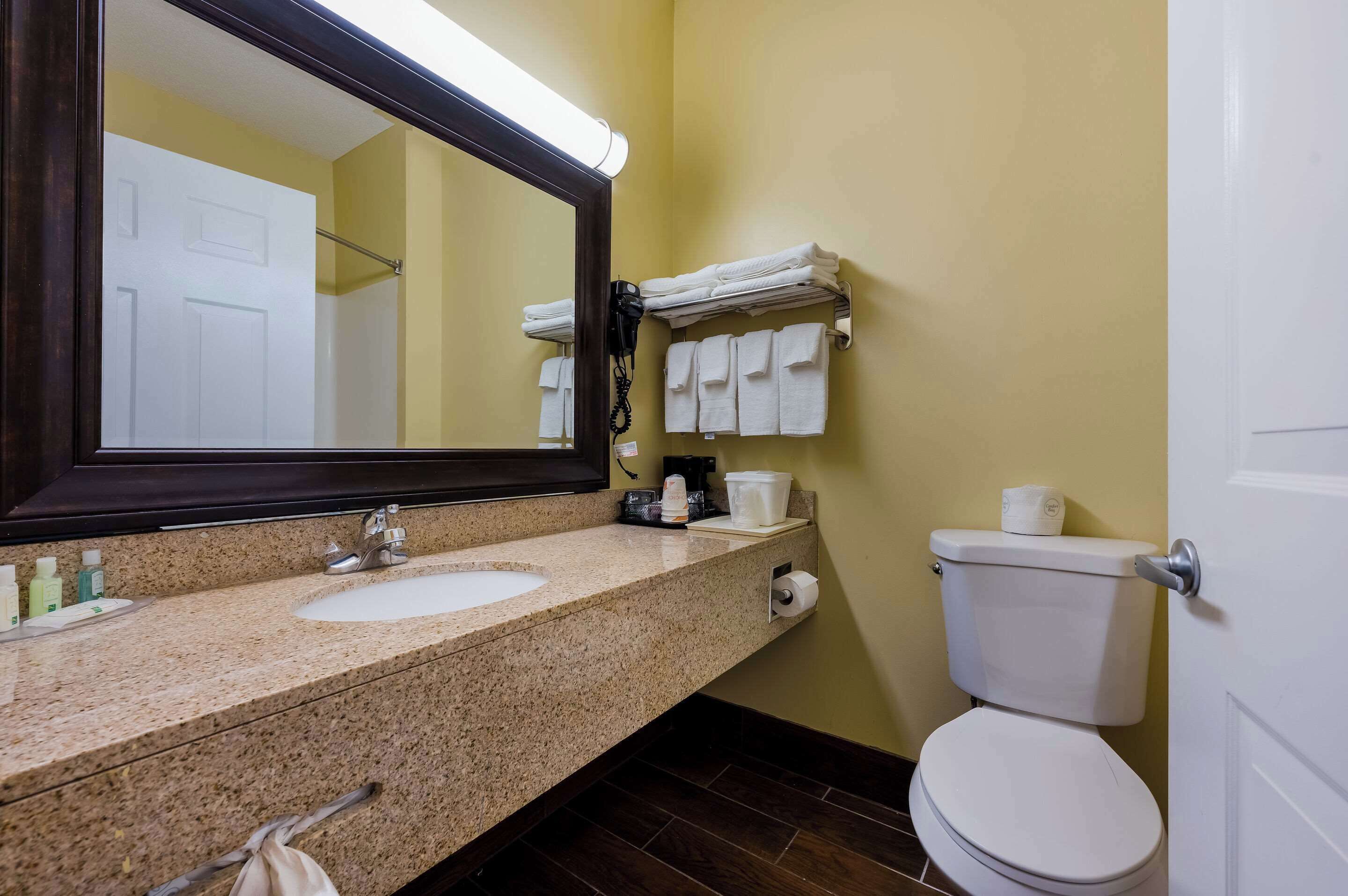 A bathroom with two sinks, a toilet, a towel rack with towels, a mirror, and a toilet paper holder.