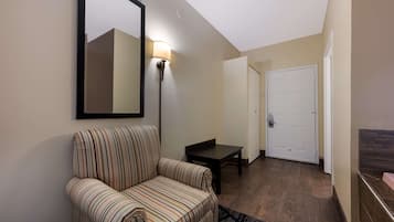A hotel room with a striped armchair, a small table, a wall-mounted lamp, and a door in the background.