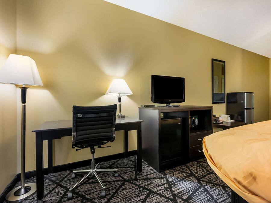 Ein Hotelzimmer mit Schreibtisch, zwei Lampen, einem Fernseher, einer Minibar und einem Bett.