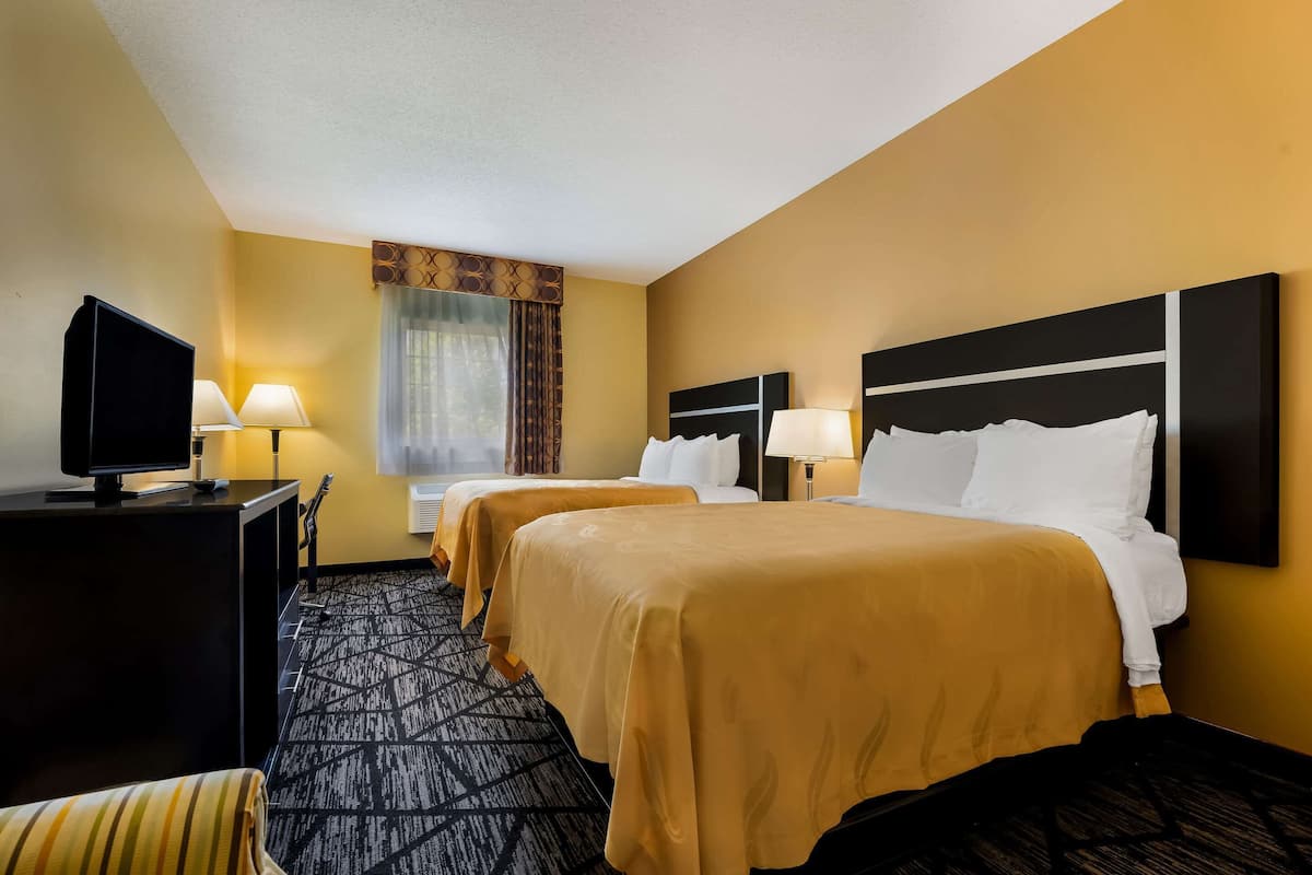 A hotel room with two beds, a TV, and a desk.