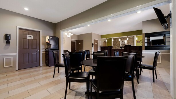 A dining area with a round table and black chairs, a refrigerator, and a door marked with accessibility symbols. - Quality Inn Fort Payne (Fort Payne)