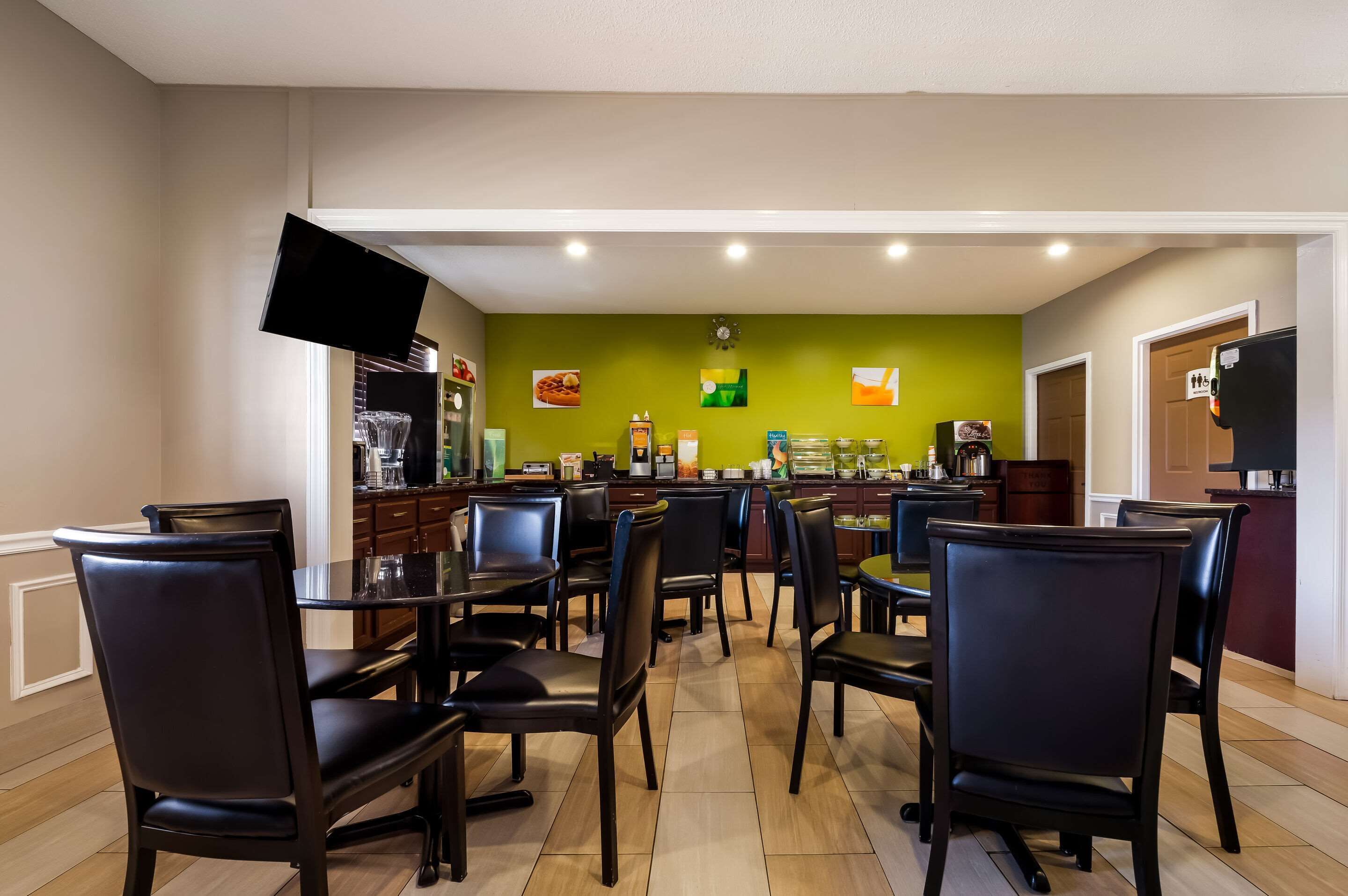 Un espace repas avec plusieurs tables et chaises, un téléviseur à écran plat fixé au mur et un coin cuisine à l’arrière-plan.