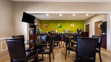 Un espace repas avec plusieurs tables et chaises, un téléviseur à écran plat fixé au mur et un coin cuisine à l’arrière-plan.