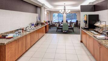 A modern kitchen with granite countertops, wooden cabinets, and a central island. There is a dining area with a chandelier and a large window providing natural light.