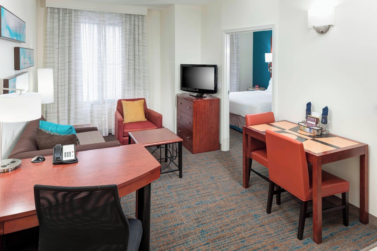 A hotel room with a living area, a dining table, a TV, a sofa, and a desk.