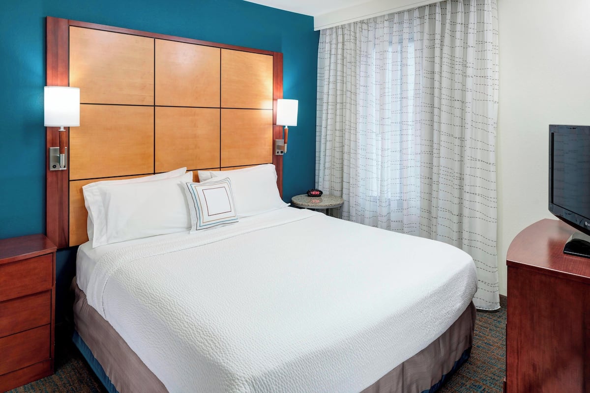 A hotel room with a large bed, two bedside lamps, a small round table, and a television on a wooden stand.