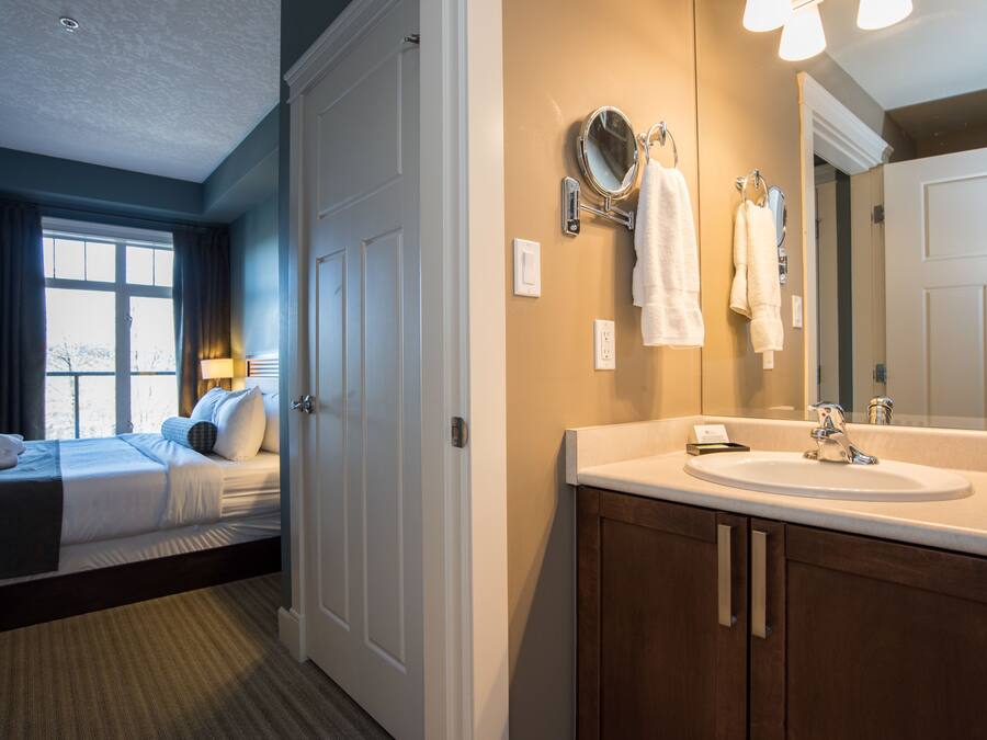 A hotel room with a bed, a bathroom with a sink and mirror, and a window with curtains.