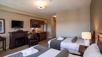 A hotel room with two beds, a television, a fireplace, a desk, and a kitchenette.