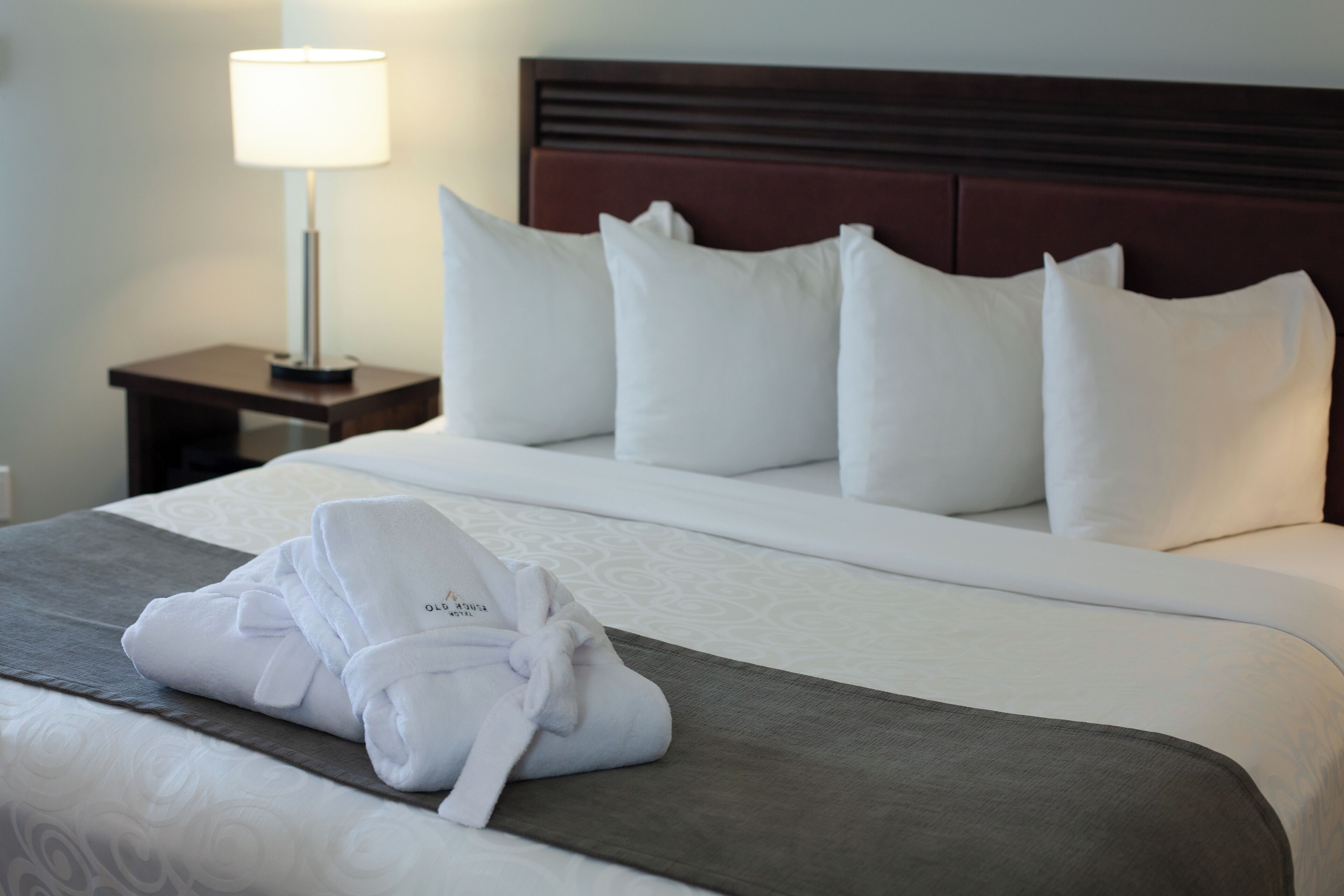 Un lit bien fait, avec du linge de lit blanc, une robe pliée posée sur le lit et une table de chevet avec une lampe à côté.