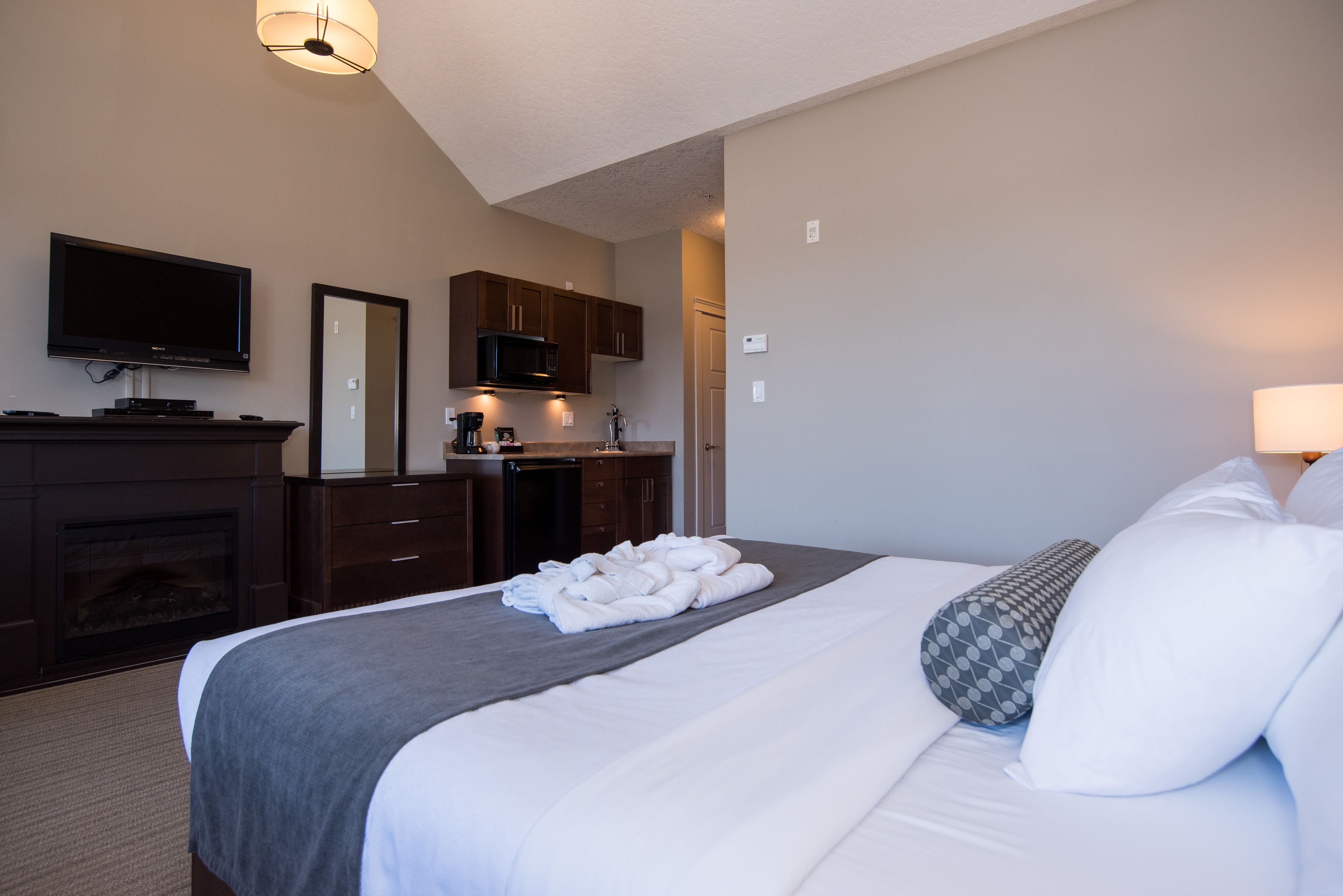A hotel room with a large bed, a flat-screen TV, a fireplace, a kitchenette, and a bathroom.