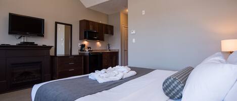 A hotel room with a large bed, a flat-screen TV, a fireplace, a kitchenette, and a bathroom.