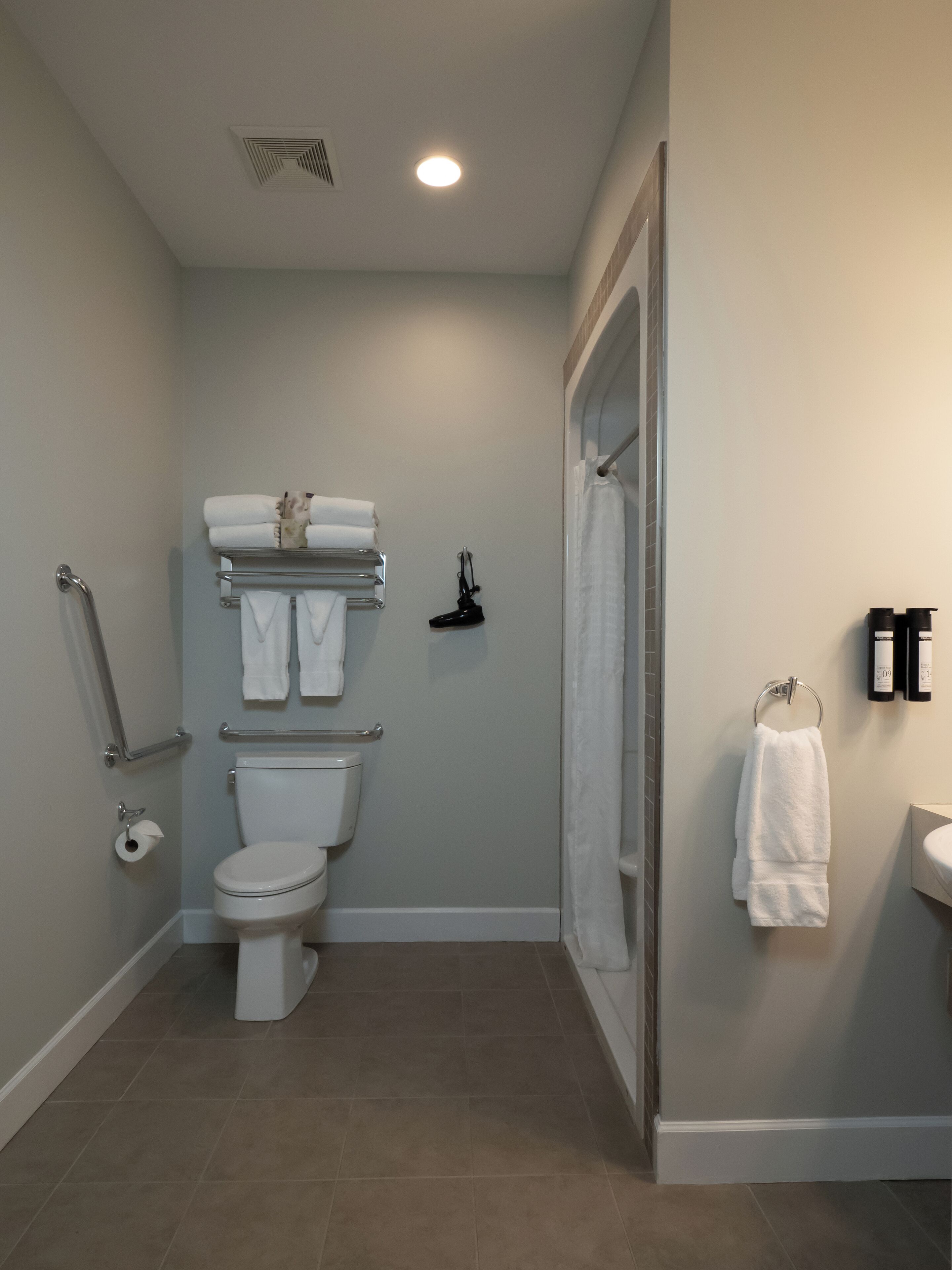 A modern bathroom with a toilet, towel rack, shower curtain, and a small shelf with toiletries.