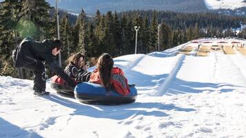Ett snötäckt landskap med en skidlift och en person som hjälper passagerare på en blå pulka.