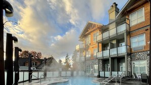 A pool area with lounge chairs, a hot tub, and a view of residential buildings. - Old House Hotel  (Courtenay)