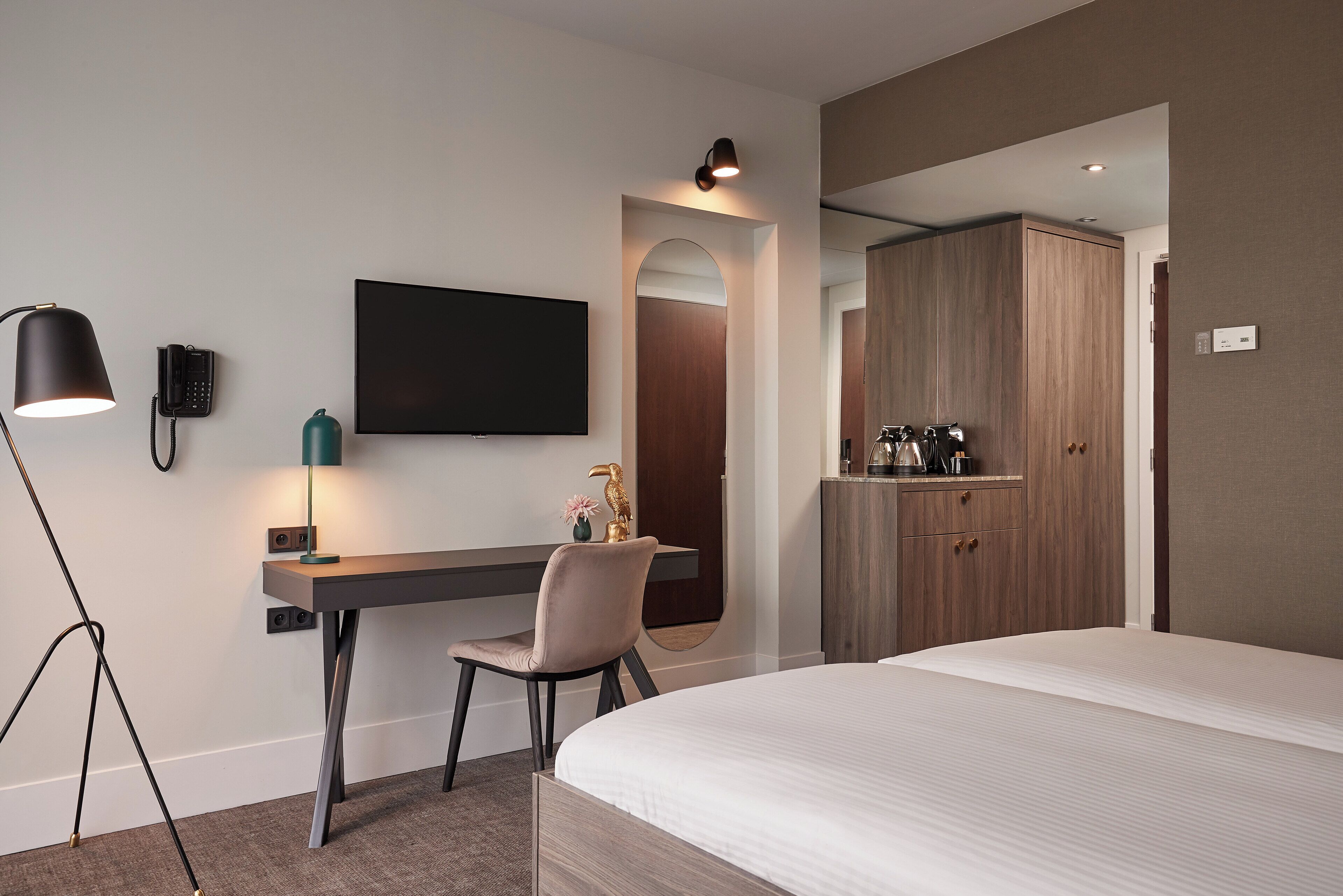 Une chambre d’hôtel moderne équipée d’un lit, d’un bureau avec une chaise, d’un téléviseur à écran plat, d’un téléphone et d’une armoire.